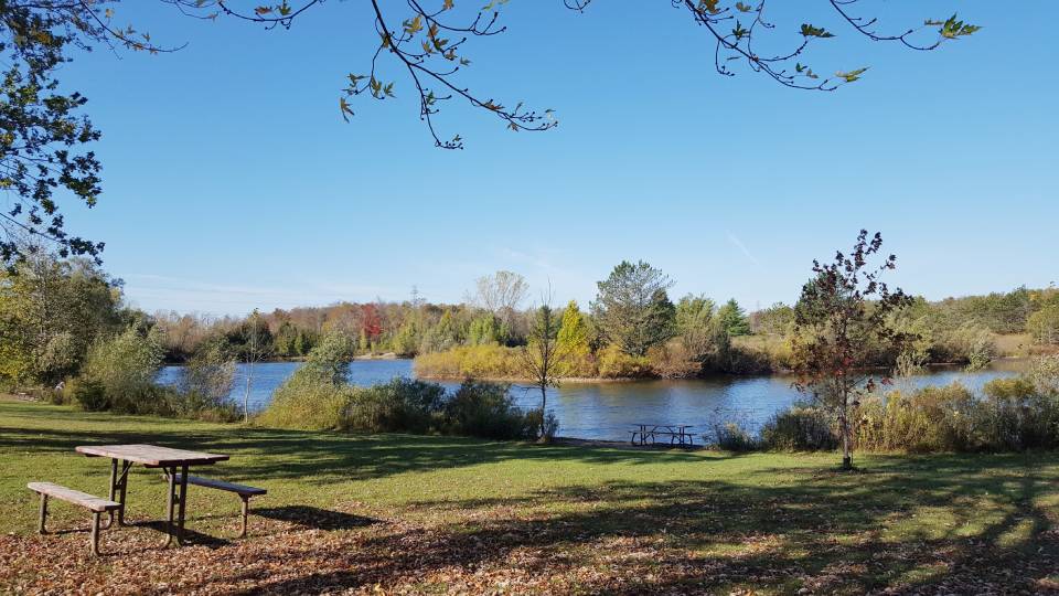 A view of a lake from a small hill, with a picnic bench beside.